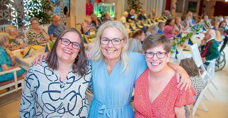Foto på Pia, Jeanette och Åsa i förgrunden med festdeltagarna vid långborden i bakgrunden.